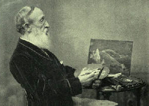 A black and white photograph of a white man seated facing to the right. He holds a paint pallet and paint brush in his hands. He sits before a small table with a small landscape painting propped up.