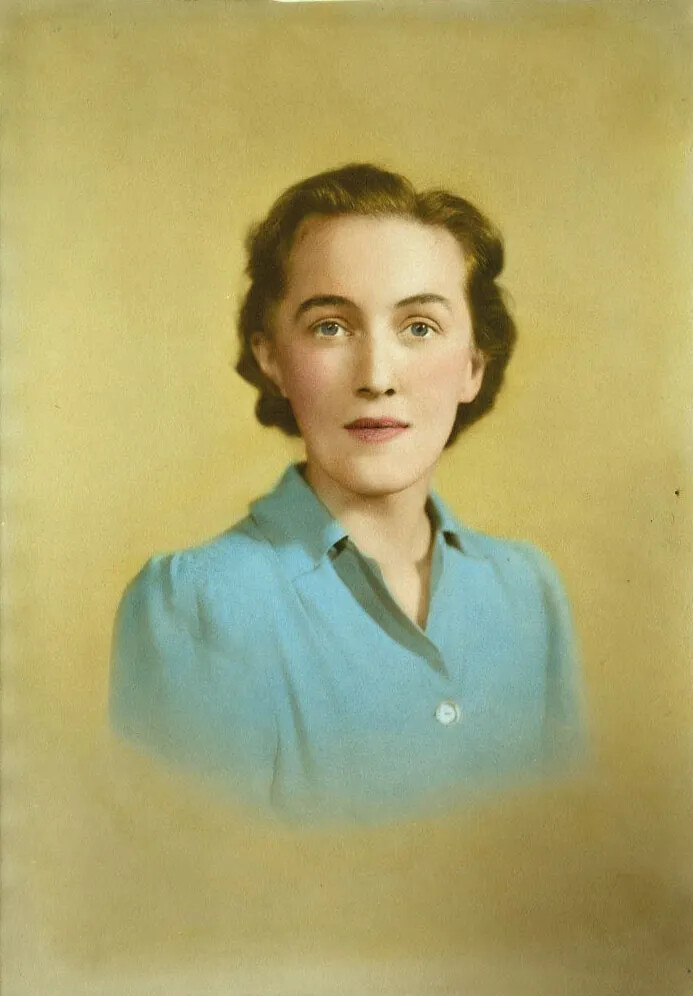 A colored photograph of a white woman looking at the viewer. She has short brown hair and wears a light blue collared shirt.