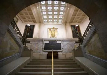 Grand staircase leading up to a golden eagle sculpture under a decorative ceiling.