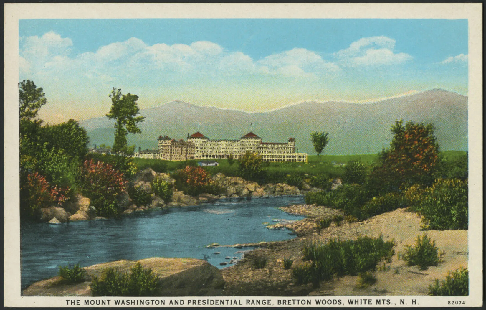 A colored postcard of a large white building with red roofs capping its two main towers. The building sits towards the back of the postcard, with a mountain range in the background. In front of the building, a green and rocky landscape surround a river, which runs through the postcard’s center. The title of the postcard, displayed along the base of the postcard, reads “THE MOUNT WASHINGTON AND PRESIDENTIAL RANGE, BRETTON WOODS, WHITE MTNS., N. H”.