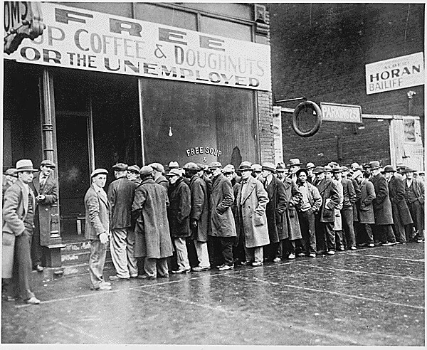 A black and white photograph of a long line of men waiting outside to enter a building.