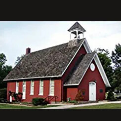 A red one-room schoolhouse with a bell tower and white-trimmed windows.