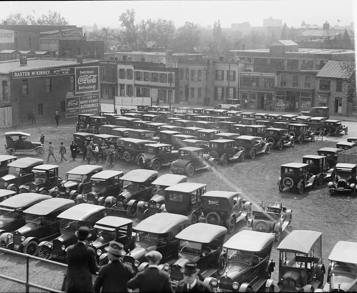A black and white photograph of a parking lot with several rows of old fashioned cars.